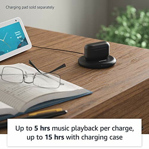 Wireless earbuds charging on a pad next to a tablet and glasses on a desk.