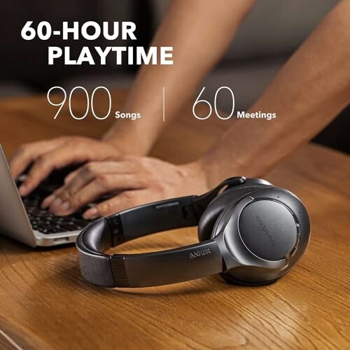 Wireless headphones on a table beside a person using a laptop.