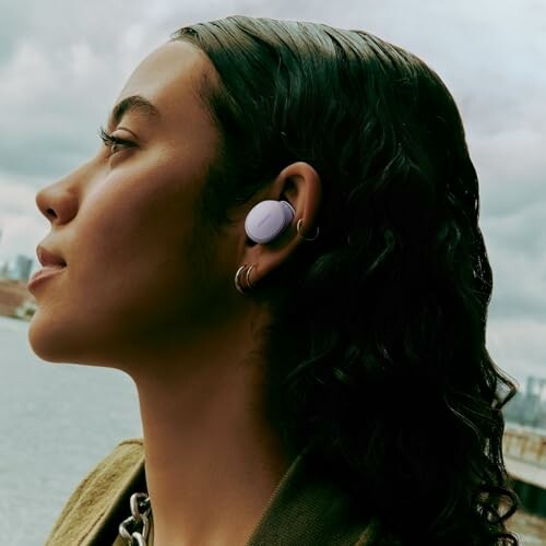 Side profile of a woman wearing wireless earbuds outdoors.