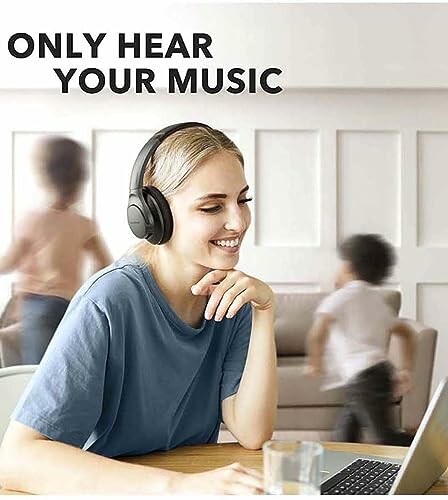 Woman wearing headphones smiling at laptop with children playing in the background.